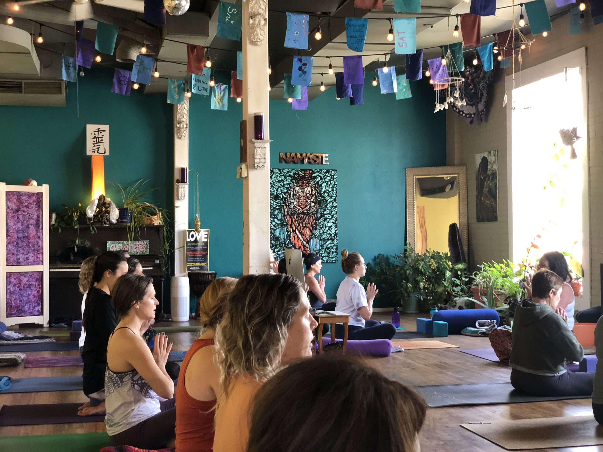 Karma Yoga Center studio interior with teal walls, colorful prayer flags, sacred art, and students in practice
